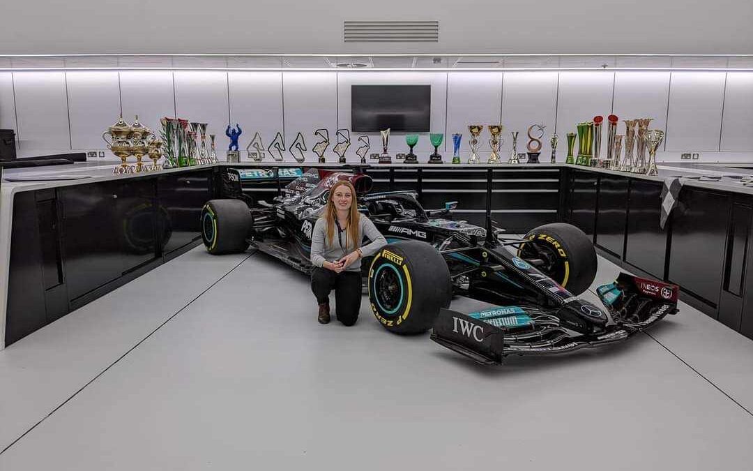 Michelle Bryant crouching to the left of a Mercedes F1 car